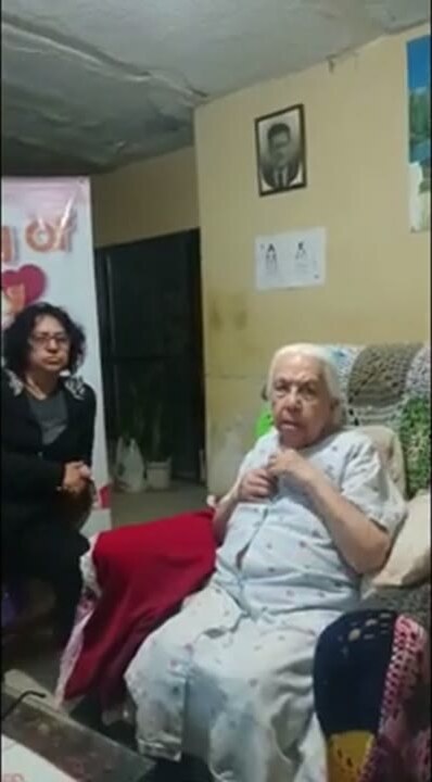 Conchita seated in her living room with a member of the Joy of Giving team beside her.