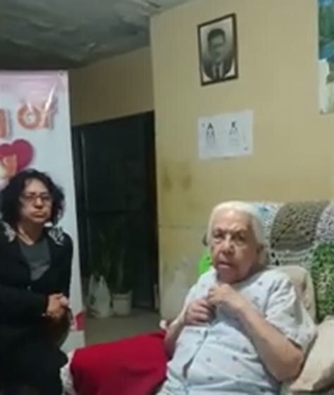Conchita seated at home, raising her hand toward her shoulder.