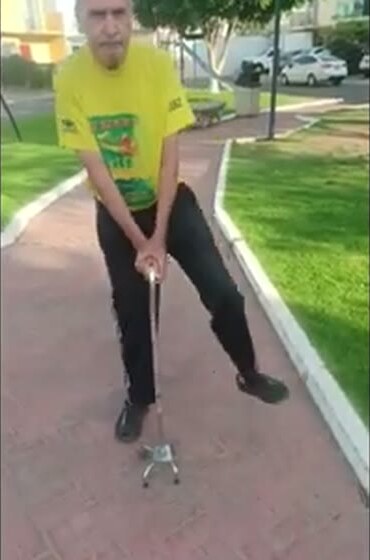Luis walking outdoors on a paved path, using a cane.