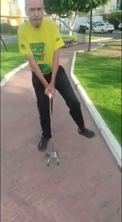 Luis standing outdoors on a garden path, walking with a cane.